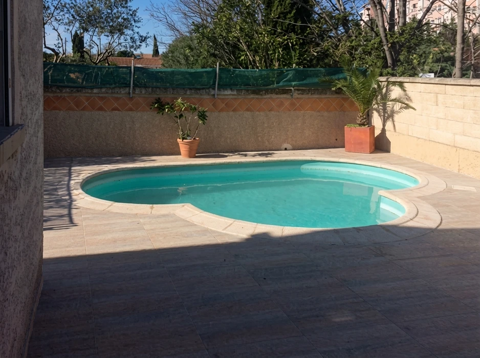 Piscine coque polyester en forme de haricot, eau turquoise, entourée d'une plage en dallage travertin beige