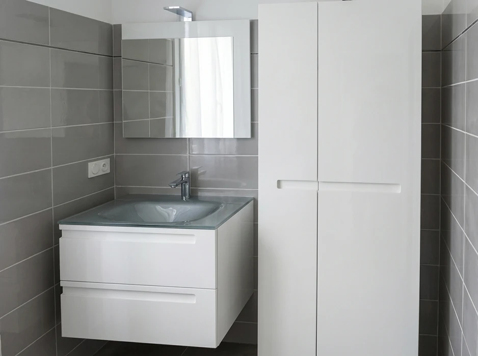 Deux artisans en combinaisons noires et t-shirts orange installent un meuble dans une salle de bain moderne aux murs en marbre blanc