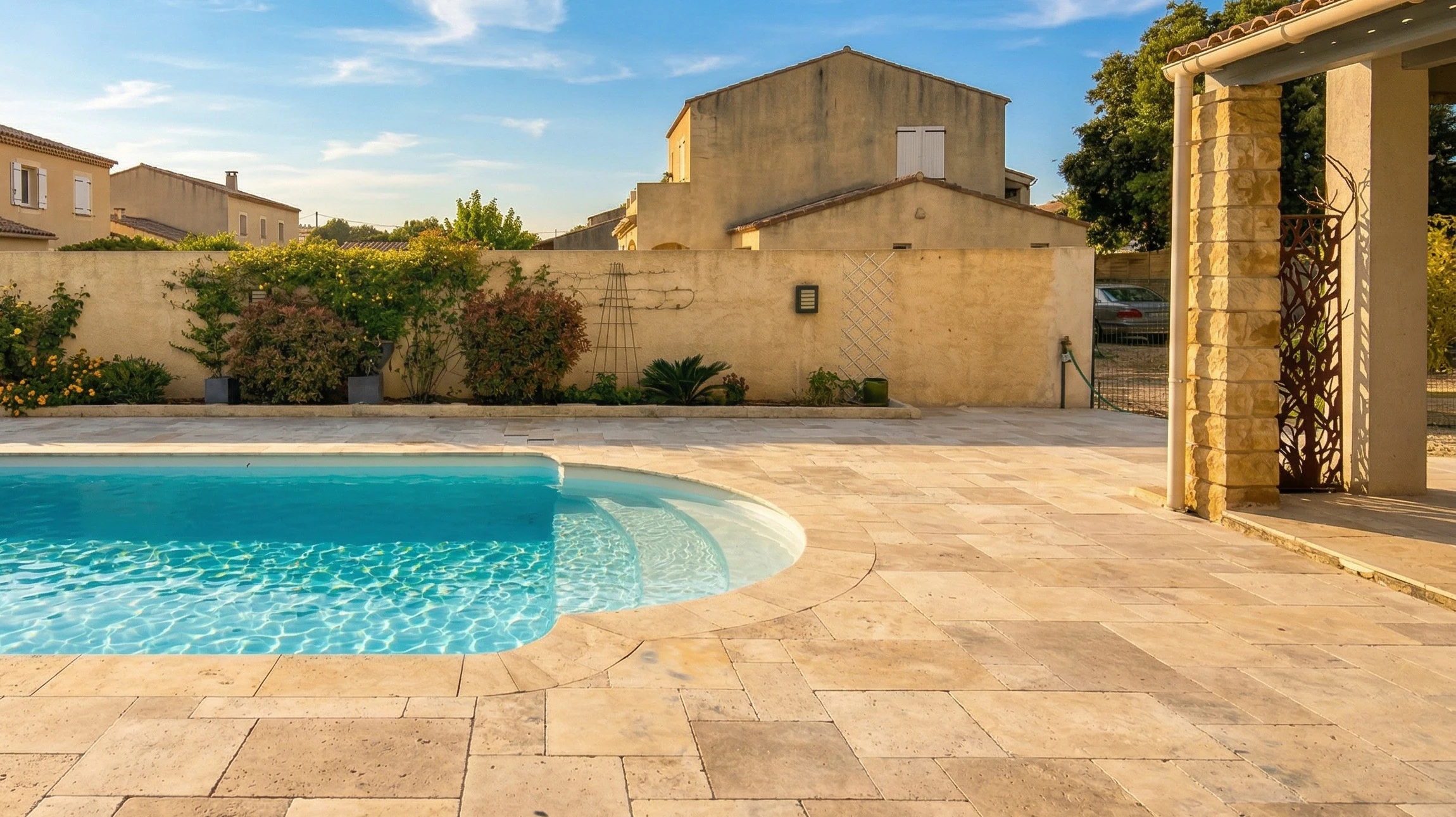 Terrasse extérieure en carrelage travertin beige entourant une piscine à fond blanc aux reflets turquoise, avec un roman step semi-circulaire