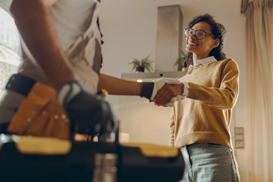 Professionnelle immobilière accueillant un couple de clients devant l'entrée d'une maison moderne